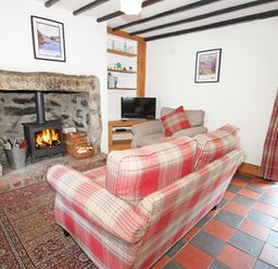 A sitting room with a fireplace a wood stove a plaid sofa and armchair a rug and a television at Ivy House in Beddgelert