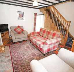 A living room with a plaid sofa armchairs a TV on a wooden stand a patterned rug and wooden stairs at Ivy House in Beddgelert