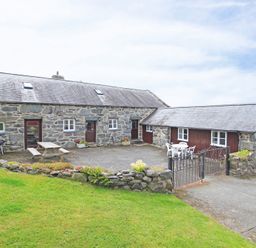 A stone cottage with two wooden doors two tables with chairs and a small stone wall at Y Beudy The Old Byre in Llanbedr