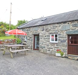 A stone cottage exterior with a picnic table and red umbrella on a concrete patio at Y Beudy The Old Byre in Llanbedr