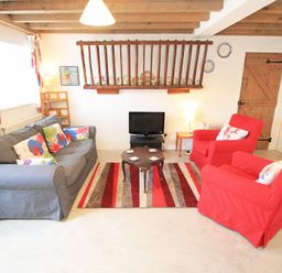 A living room with a gray sofa, red armchairs, a small round table, and a TV at Y Beudy The Old Byre in Llanbedr