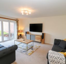 A living room with two dark sofas yellow pillows a wooden coffee table a TV on a wooden sideboard a lamp and sliding glass doors at 4 Centurion Rise in Penrith