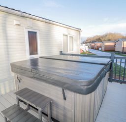 A covered hot tub on a deck attached to a building with small stairs and other similar buildings nearby at Downtime Lodge near Felton