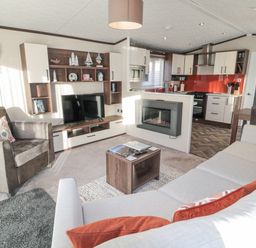 A living room with a sofa and armchair a TV mounted on a wooden wall unit a coffee table a fireplace and a kitchen with dining area at Downtime Lodge near Felton