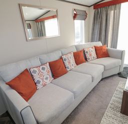 A living room with a light gray sofa with orange and patterned cushions near windows with gray curtains and a coffee table at Downtime Lodge near Felton