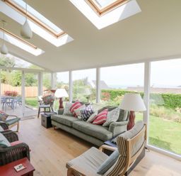 A sunroom with multiple chairs sofa and table lamps overlooking a garden at Tree Tops in Newport Pembrokeshire