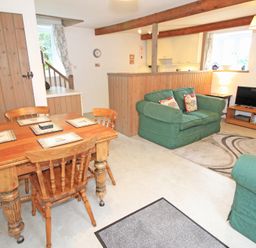 A living room and dining area with wooden table and chairs green sofas television and kitchen at Y Stabl The Old Stable in Llanbedr