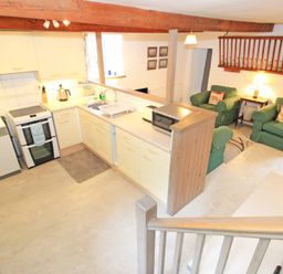 A kitchen with white cabinets stove dishwasher and microwave next to a sitting area with green armchairs and a lamp at Y Stabl The Old Stable in Llanbedr
