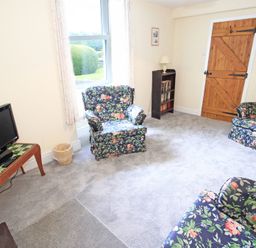 A sitting room with floral armchairs a wooden door a television on a table and a small bookshelf at The Farmhouse in Llanbedr