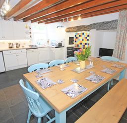 A kitchen dining area with a wooden table and blue chairs and a tiled backsplash at The Farmhouse in Llanbedr