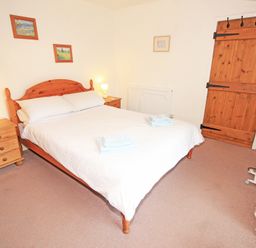 A bedroom with a wooden double bed white bedding bedside tables lamps wooden door and carpet at The Farmhouse in Llanbedr