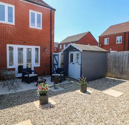 A backyard with gravel ground a small patio area with table chairs two armchairs a fire pit a shed and potted plants at Ty Bach Twt Llanelli