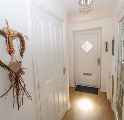 A hallway with a white front door a wooden floor a decorative heart hanging on the wall and a glass-paneled door at Ty Bach Twt Llanelli