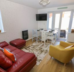 A living room with a red leather sofa an ottoman a yellow armchair a white dining table with chairs and a wall-mounted television at Ty Bach Twt Llanelli