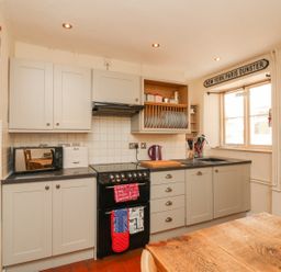 A kitchen with grey cabinets a black stove and a wooden table at Little Dragons in Dunster near Minehead