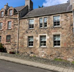 A stone residential building with multiple sash windows a sidewalk and a wooden gate at 49 Castlegate in Jedburgh