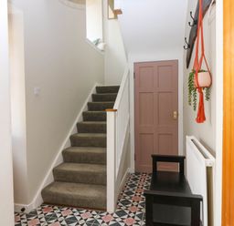 A hallway with patterned tile floor a staircase a wooden door a black bench and a hanging plant at 49 Castlegate in Jedburgh