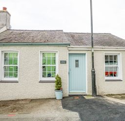 A exterior view of a small beige cottage with two windows a blue front door a potted plant and a street lamp at Pippin Cottage in Beaumaris