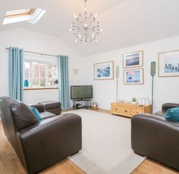 A living room with two brown leather sofas a TV on a stand blue curtains and framed pictures on the wall at Pippin Cottage in Beaumaris