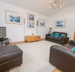 A living room with two brown leather sofas a brown leather ottoman a wooden coffee table a television on a black stand and framed pictures on the wall at Pippin Cottage in Beaumaris