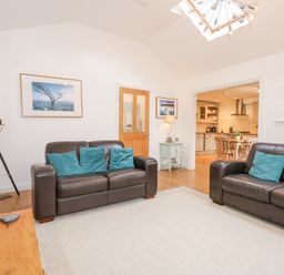 A living room with two brown leather sofas with blue cushions a tripod lamp and a wooden door leading to a kitchen at Pippin Cottage in Beaumaris