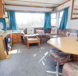A living room with a corner sofa and blue curtains at Tanyfron Holiday Caravan in Bryngwran near Gwalchmai
