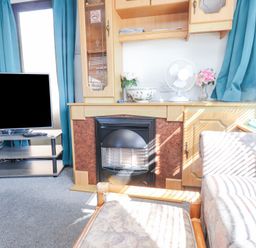 A living room with a television on a stand a fireplace and couches with blue curtains at Tanyfron Holiday Caravan in Bryngwran near Gwalchmai
