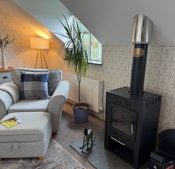 A snug with an armchair, ottoman, stove, and plant at The Hayloft in Lostwithiel
