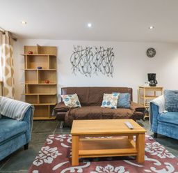 A living room with blue armchairs a brown sofa and a wooden coffee table at Oak Cottage in Aylesbeare
