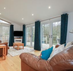 A living room with brown leather sofas wooden tables a television and large glass doors leading outside at 2 Miller's Island Near Lanreath