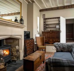 A living room with a fireplace wood stove and wooden furniture including a sofa chair and chest at Courtyard House in Blockley