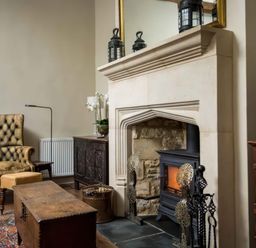 A living room with a stone fireplace a wood-burning stove an armchair and wooden furniture at Courtyard House in Blockley
