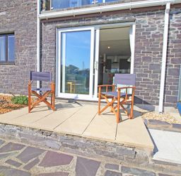 An outdoor patio area with two wooden chairs in front of sliding glass doors at Harbour Escape in Porthmadog
