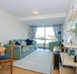A living room with green sofa blue cushions wooden dining table and chairs shelving unit and glass doors with curtains at Harbour Escape in Porthmadog