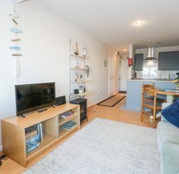 A living room with a sofa a TV on a wooden stand a dining table with chairs and a kitchen area at Harbour Escape in Porthmadog