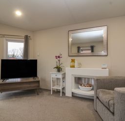 A living room with a television on a stand a small white side table a gray armchair and a fireplace with a mirror above it at Longdon Lodge in Wickhamford near Evesham