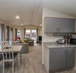 An open-plan kitchen and dining area with gray cabinets and a dining table with chairs next to a living room with armchairs and a television at Longdon Lodge in Wickhamford near Evesham