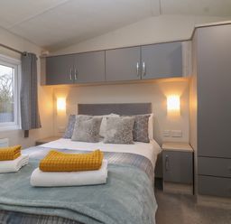 A bedroom with a bed with pillows and folded towels next to a window and gray cabinets at Longdon Lodge in Wickhamford near Evesham