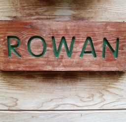 A wooden sign with the word Rowan engraved on it placed on a wooden surface at Rowan Lodge in Rosliston