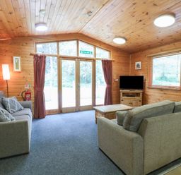 A wooden living room with two gray sofas a wooden coffee table a TV on a wooden stand and large glass doors at Oak Lodge in Rosliston