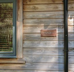 A wooden cabin wall with a window and a sign that says oak at Oak Lodge Rosliston
