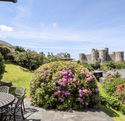 A garden with flowering bush and patio furniture overlooking a castle at Bryn Awelon in Harlech