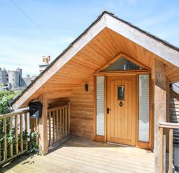 A wooden porch with a front door and railing with a castle in the background at Bryn Awelon in Harlech