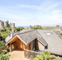 A house with a wooden deck and slate roof near a large stone castle and countryside at Bryn Awelon in Harlech