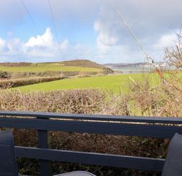 A balcony with two chairs overlooking green fields hills and a body of water at Little Trevorrick Caravan in St Issey
