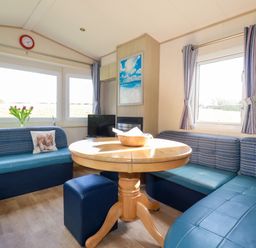 A dining area with a round wooden table surrounded by blue cushioned seating and a small TV at Little Trevorrick Caravan in St Issey
