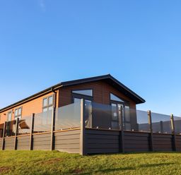 A wooden lodge with glass panel fencing on a grassy area at Cherry Blossom Lodge in Whitby