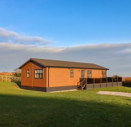 A single story wooden house with windows and a small porch on a grassy plot at Cherry Blossom Lodge in Whitby