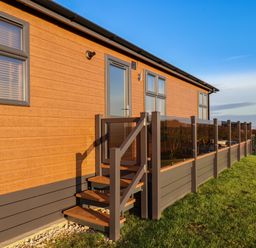 An exterior view of a wooden building with steps leading to a door and a railing on a grassy area at Cherry Blossom Lodge in Whitby