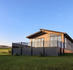 A wooden cabin with glass balcony on a grassy lawn under a clear blue sky at Holly Lodge in Whitby